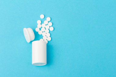 İlaç şişesi ve beyaz haplar mavi renkli arka plana dökülmüş. İlaç ve reçeteli haplar.