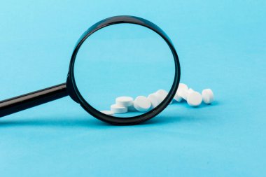 Büyüteç kullanarak hapları yakınlaştırıyorum. Özel benzersiz haplar mavi arka planda izole edilmiş.