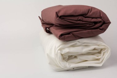 Katlanmış beyaz ve kestane rengi yatak çarşafları ve beyaz yastık kılıfları yığını; arkaplan; yakın plan.