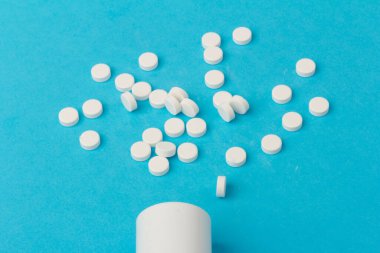 İlaç şişesi ve beyaz haplar mavi renkli arka plana dökülmüş. İlaç ve reçeteli haplar.