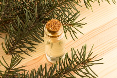 Tahta bir masanın üzerinde köknar dalları olan bir şişe köknar yağı.