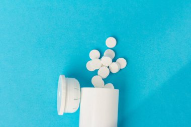 İlaç şişesi ve beyaz haplar mavi renkli arka plana dökülmüş. İlaç ve reçeteli haplar.