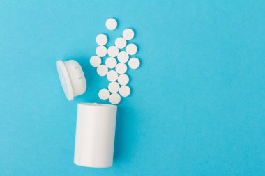 İlaç şişesi ve beyaz haplar mavi renkli arka plana dökülmüş. İlaç ve reçeteli haplar.