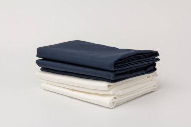 Beyaz üzerine katlanmış beyaz ve mavi yatak çarşafları ve yastık kılıfları yığını; arkaplan; kapanış.