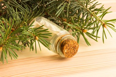 Tahta bir masanın üzerinde köknar dalları olan bir şişe köknar yağı.