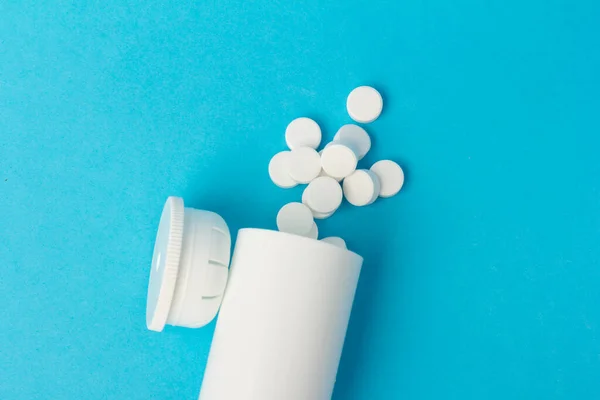 Medication bottle and white pills spilled on blue pastel coloured background. Medication and prescription pills.