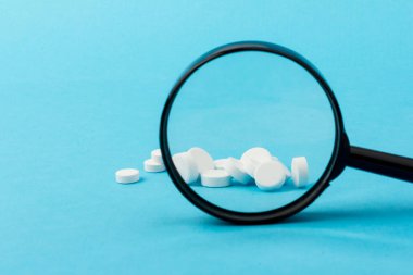 Büyüteç kullanarak hapları yakınlaştırıyorum. Özel benzersiz haplar mavi arka planda izole edilmiş.