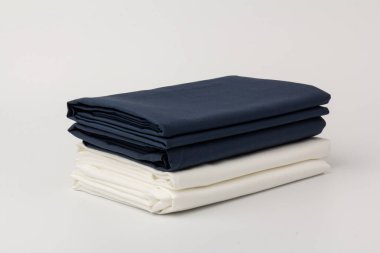 Beyaz üzerine katlanmış beyaz ve mavi yatak çarşafları ve yastık kılıfları yığını; arkaplan; kapanış.