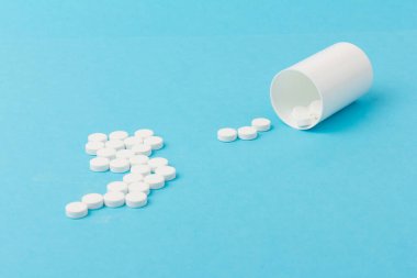İlaç şişesi ve beyaz haplar mavi renkli arka plana dökülmüş. İlaç ve reçeteli haplar.