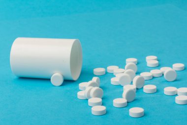 İlaç şişesi ve beyaz haplar mavi renkli arka plana dökülmüş. İlaç ve reçeteli haplar.