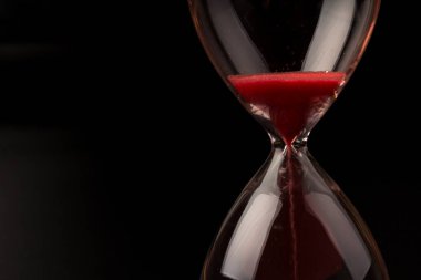 Kırmızı Kum, bir kum saatinin ampullerinin içinden geçerek bir geri sayım bitimine kadar geçen zamanı ölçüyor, fotokopi alanı olan siyah bir arkaplanda..