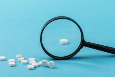 Büyüteç kullanarak hapları yakınlaştırıyorum. Özel benzersiz haplar mavi arka planda izole edilmiş.