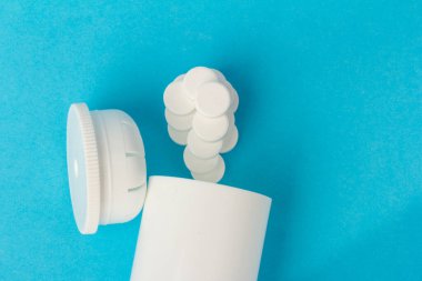 İlaç şişesi ve beyaz haplar mavi renkli arka plana dökülmüş. İlaç ve reçeteli haplar.