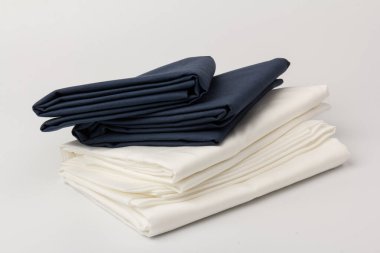 Beyaz üzerine katlanmış beyaz ve mavi yatak çarşafları ve yastık kılıfları yığını; arkaplan; kapanış.