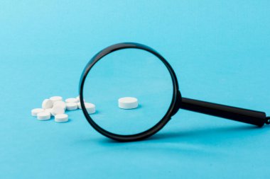 Büyüteç kullanarak hapları yakınlaştırıyorum. Özel benzersiz haplar mavi arka planda izole edilmiş.