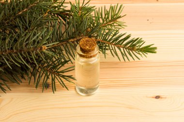 Tahta bir masanın üzerinde köknar dalları olan bir şişe köknar yağı.