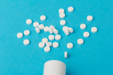 İlaç şişesi ve beyaz haplar mavi renkli arka plana dökülmüş. İlaç ve reçeteli haplar.