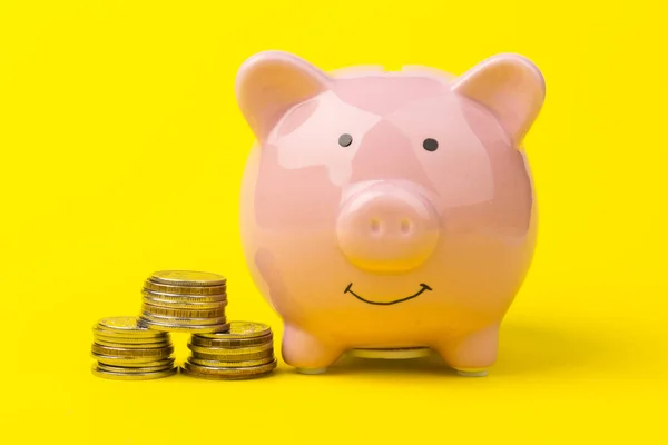 Piggy bank with coin pile on yellow background, space for text. Finance, saving money. Business to success and saving for retirement concept