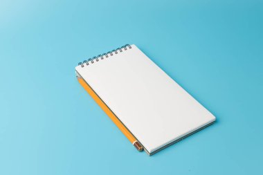 Mavi arkaplanda kurşun kalemle birlikte açık spiral boş defterin üst görünümü 