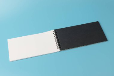 Mavi arkaplandaki açık spiral beyaz ve siyah defterin üst görünümü 