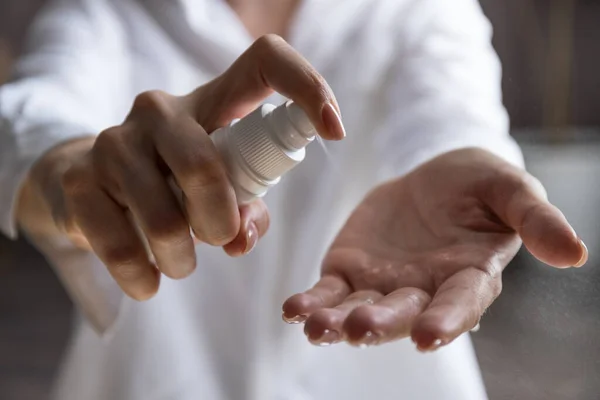 Woman applying spray disinfection alcohol product on hand. Disinfecting hands against virus bacteria, health prevention in day at home or work.