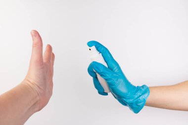 Mavi nitril eldivenli bir kişinin eli, Covid-19 salgını sırasında enfeksiyonu önlemek ve sağlığı korumak için korumasız bir kişinin eline dezenfektan sıkar..