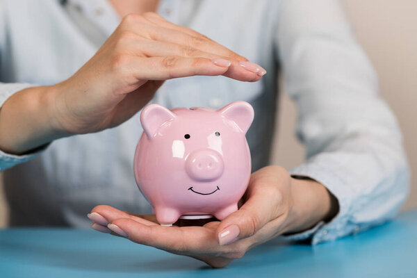 Piggy bank in hands on blue background, space for text. Finance, saving money