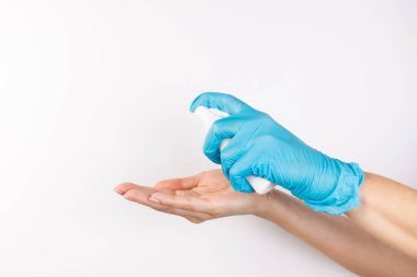 Mavi nitril eldivenli bir kişinin eli, Covid-19 salgını sırasında enfeksiyonu önlemek ve sağlığı korumak için korumasız bir kişinin eline dezenfektan sıkar..