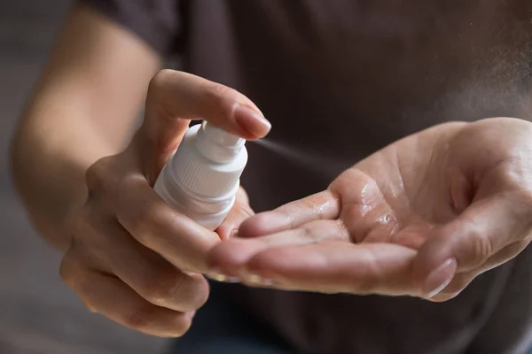 Woman applying spray disinfection alcohol product on hand. Disinfecting hands against virus bacteria, health prevention in day at home or work.