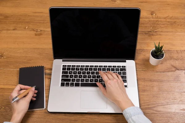 woman working with laptop on old wood table in modern coffee shop or loft. Mix of office supplies and gadgets on a wooden desk background. copy space.