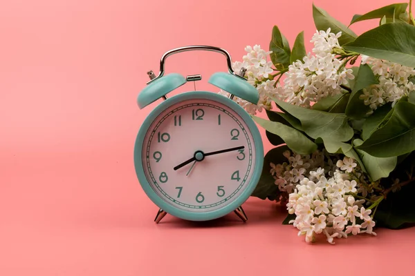 蓝色的老式闹钟 白色紫丁香花 粉红色背景隔离 春天的时间变化 春天的花朵和闹钟 — 图库照片