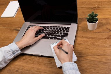 Eski ahşap masada dizüstü bilgisayarla çalışan bir kadın. Ahşap masa arkasında ofis malzemeleri ve aletlerin karışımı. Boşluğu kopyala.