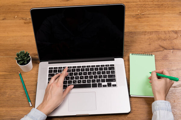 Woman working with laptop on old wood table. Mix of office supplies and gadgets on a wooden desk background. copy space.