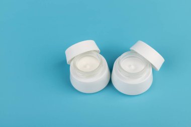 Mavi arka planda nemlendirici yüz kremi kabı. Moda kadını hala hayatta. Pop kadın şeyleri, ilaç ve kozmetik tema.