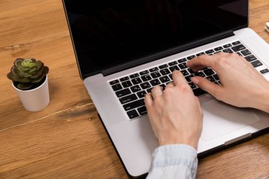 Eski ahşap masada dizüstü bilgisayarla çalışan bir kadın. Ahşap masa arkasında ofis malzemeleri ve aletlerin karışımı. Boşluğu kopyala.