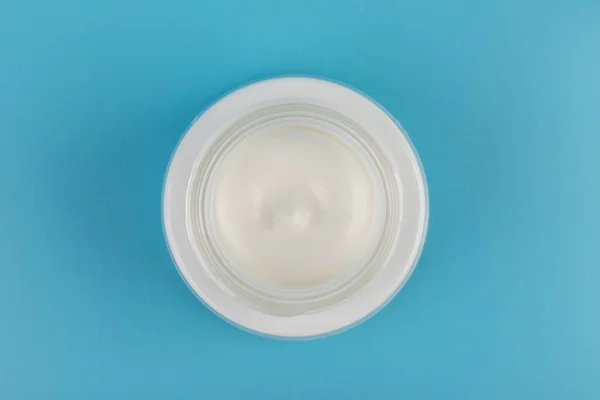 Mavi arka planda nemlendirici yüz kremi kabı. Moda kadını hala hayatta. Pop kadın şeyleri, ilaç ve kozmetik tema.