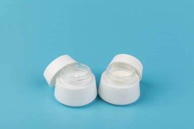 Mavi arka planda nemlendirici yüz kremi kabı. Moda kadını hala hayatta. Pop kadın şeyleri, ilaç ve kozmetik tema.