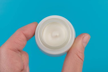 Mavi arka planda nemlendirici yüz kremi kabı. Moda kadını hala hayatta. Pop kadın şeyleri, ilaç ve kozmetik tema.