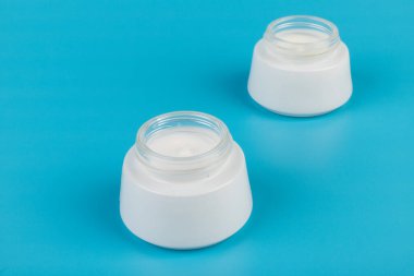 Mavi arka planda nemlendirici yüz kremi kabı. Moda kadını hala hayatta. Pop kadın şeyleri, ilaç ve kozmetik tema.