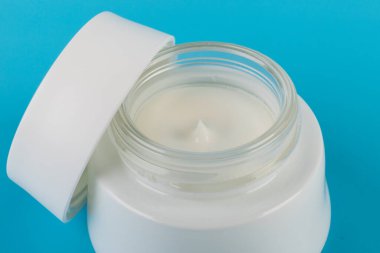 Mavi arka planda nemlendirici yüz kremi kabı. Moda kadını hala hayatta. Pop kadın şeyleri, ilaç ve kozmetik tema.