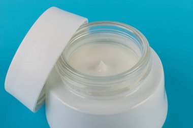Mavi arka planda nemlendirici yüz kremi kabı. Moda kadını hala hayatta. Pop kadın şeyleri, ilaç ve kozmetik tema.