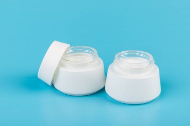 Mavi arka planda nemlendirici yüz kremi kabı. Moda kadını hala hayatta. Pop kadın şeyleri, ilaç ve kozmetik tema.