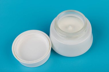 Mavi arka planda nemlendirici yüz kremi kabı. Moda kadını hala hayatta. Pop kadın şeyleri, ilaç ve kozmetik tema.