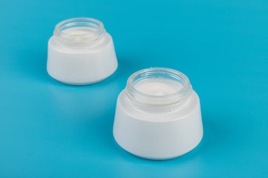Mavi arka planda nemlendirici yüz kremi kabı. Moda kadını hala hayatta. Pop kadın şeyleri, ilaç ve kozmetik tema.