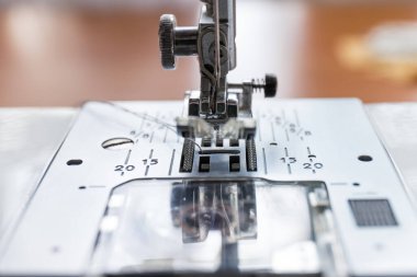 Dikiş bezi için endüstriyel dikiş makinesinin koyu ipliğine sahip iğne basan ayak ve fotokopi alanı yakın plan ile bulanık bokeh arkaplan.