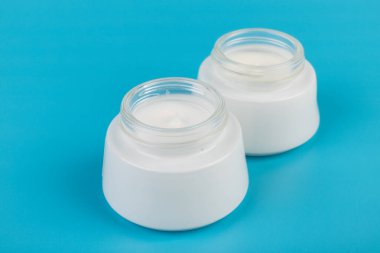 Mavi arka planda nemlendirici yüz kremi kabı. Moda kadını hala hayatta. Pop kadın şeyleri, ilaç ve kozmetik tema.