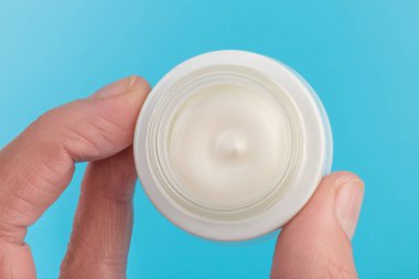 Mavi arka planda nemlendirici yüz kremi kabı. Moda kadını hala hayatta. Pop kadın şeyleri, ilaç ve kozmetik tema.