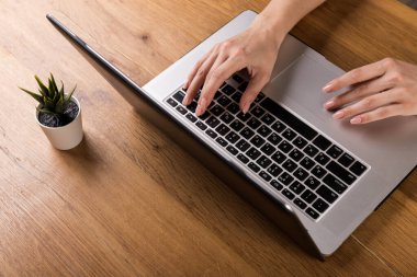 Eski ahşap masada dizüstü bilgisayarla çalışan bir kadın. Ahşap masa arkasında ofis malzemeleri ve aletlerin karışımı. Boşluğu kopyala.