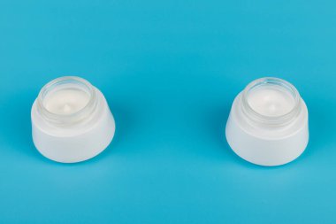 Mavi arka planda nemlendirici yüz kremi kabı. Moda kadını hala hayatta. Pop kadın şeyleri, ilaç ve kozmetik tema.