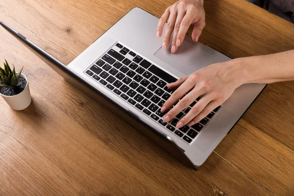 Woman working with laptop on old wood table. Mix of office supplies and gadgets on a wooden desk background. copy space.